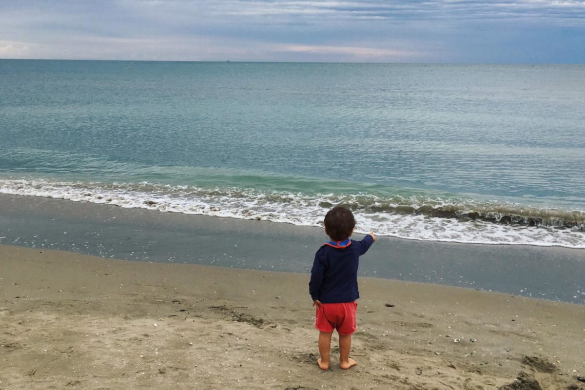 Un bambinno da solo sulla spiaggia guarda l'orizzonte