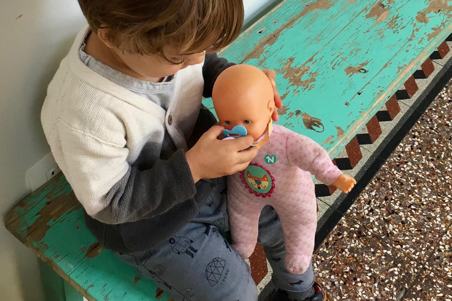 Un bambino gioca con una bambola su una panca di legno